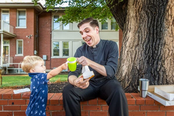 Lisa Johnston | lisajohnston@archstl.org | twitter: @aeternusphoto

Evangelizing through broadcasting his day on Twitter, Father Michael Grosch is using the #lifeasapriest to share what it is like to be a priest on an ordinary day. He shared a donut and a cup of milk with 16-month-old Dylan Schmidt, during a gathering of parents on the school parking lot on the first day of classes.

Msgr. Mike Dieckman @MsgrMike (St. Paul in Fenton), Father John Schneier @schneier791 (St. Joseph Cottleville), Father Peter Fonseca @peterjfonseca (Queen of All Saints) and Father Dan Kavanaugh @CanadanSTL (St. Patrick's in Wentzville) are also participating.